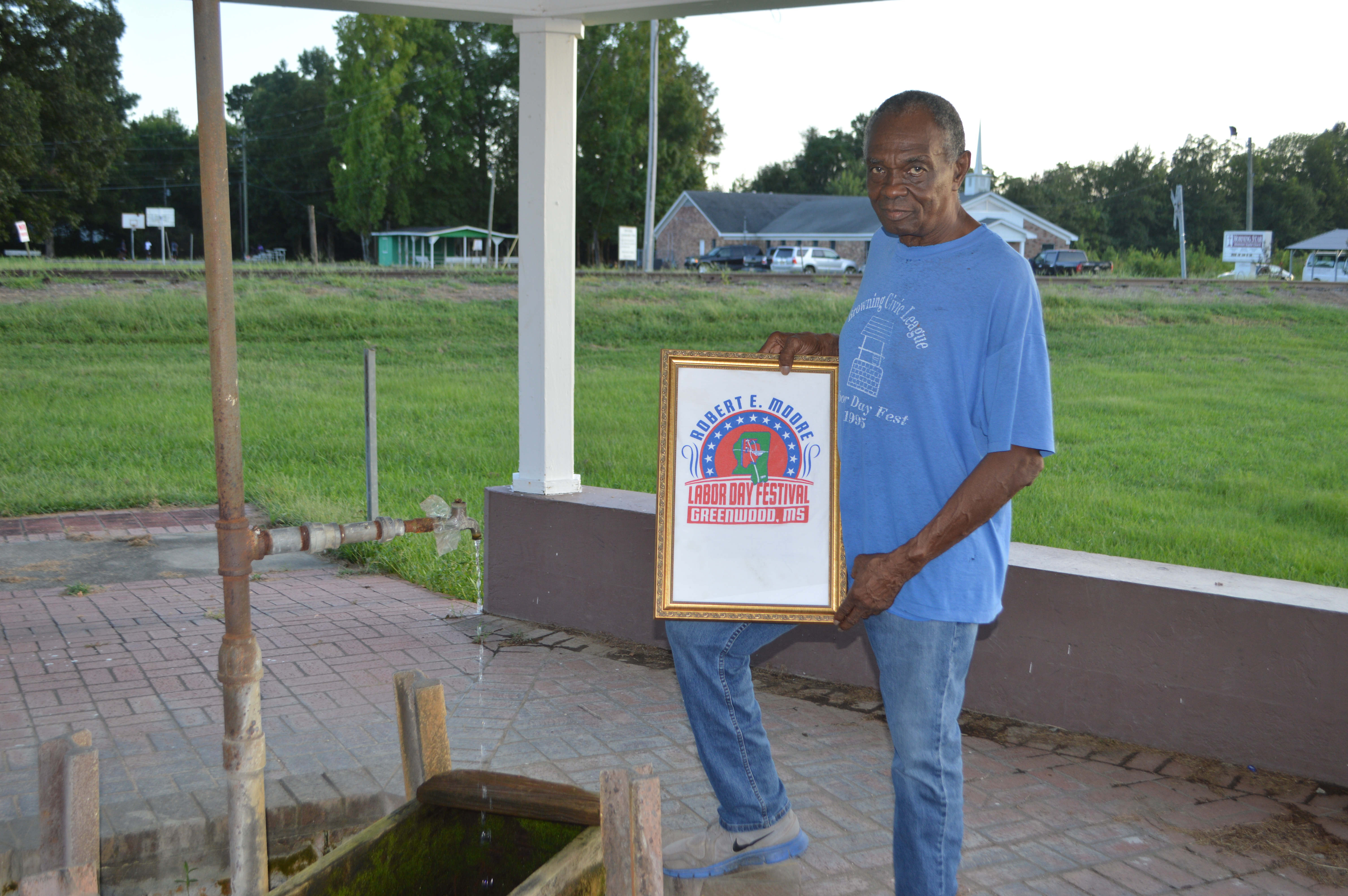 Charles Moore, a member of the Browning Progressive Civic League, holds up a sign for the Robert E. Moore Labor Day Festival, which was named after his brother, the late Robert E. Moore. He is standing at the Browning artesian well.