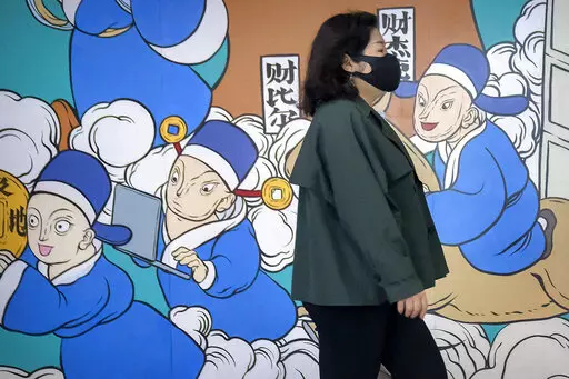 A woman wearing a face mask walks past a mural in Beijing, Friday, April 22, 2022. Officials in Shanghai promised Friday to ease anti-virus controls on truck drivers that are hampering food supplies and trade as they try to revive the local economy while millions of people are still confined to their homes. (AP Photo/Mark Schiefelbein)