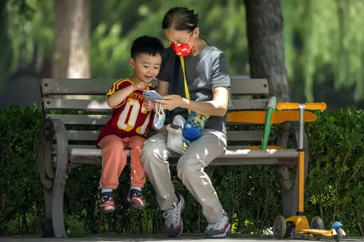 A woman wearing a face mask and a child look at a cellphone as they sit on a bench at a public park in Beijing, on June 2, 2022. As the week-long Lunar New Year holidays in China draw near with promises of feasts and red envelopes stuffed with cash, children have yet another thing to look forward to - one extra hour of online games each day. (AP Photo/Mark Schiefelbein, File)