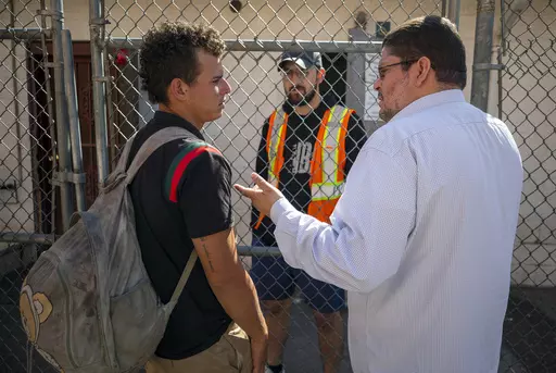 Venezuelan migrant Said Jose, left, asks for help from Jesuit priest Daniel Mora while looking his girlfriend who he got separated with during his detention, at the shelter run by the Sacred Heart Church in El Paso, Texas, Friday, May 12, 2023. The border between the U.S. and Mexico was relatively calm Friday, offering few signs of the chaos that had been feared following a rush by worried migrants to enter the U.S. before the end of pandemic-related immigration restrictions. (AP Photo/Andres Le