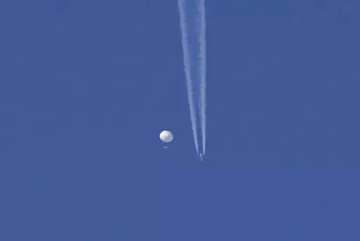 In this photo provided by Brian Branch, a large balloon drifts above the Kingstown, N.C. area, with an airplane and its contrail seen below it. The United States says it is a Chinese spy balloon moving east over America at an altitude of about 60,000 feet (18,600 meters), but China insists the balloon is just an errant civilian airshipused mainly for meteorological research that went off course due to winds and has only limited “self-steering” capabilities. (Brian Branch via AP)