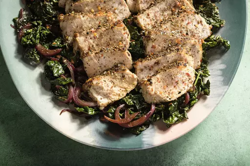 This image released by Milk Street shows a recipe for pork with kale, red wine and toasted garlic. (Milk Street via AP)