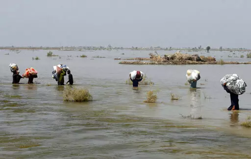 Victims of heavy flooding from monsoon rains crowd carry relief aid through flood water in the Qambar Shahdadkot district of Sindh Province, Pakistan, Sept. 9, 2022. The United Nations says weather disasters costing $200 million a day and irreversible climate catastrophe looming show the world is “heading in the wrong direction.” (AP Photo/Fareed Khan, File)