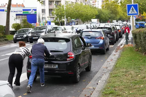 People push their car in a line of vehicles waiting to reach a station, Friday, Oct. 14, 2022 in Nanterre, outside Paris. Strikes in the French refineries of TotalEnergies group were still going on Friday, heavily disrupting fuel supplies as hard-left CGT union rejected a deal over pay rise that has been found between the energy giant and two other more moderate unions. (AP Photo/Michel Euler)
