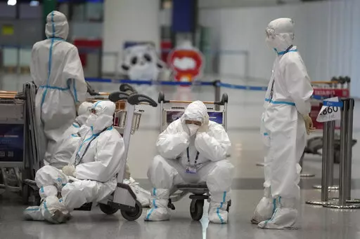 Olympic workers in protective clothing take a rest after helping travellers at Beijing Capital International airport after the 2022 Winter Olympics, Monday, Feb. 21, 2022, in Beijing, China. (AP Photo/Frank Augstein)