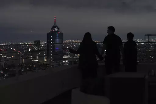 A family looks out at Mexico City from their apartment building rooftop after an earthquake early Thursday, Sept. 22, 2022. The magnitude 6.8 quake struck at 1:19 a.m. local time, causing at least two deaths, damaging buildings and setting off landslides near the epicenter in the western state of Michoacan. (AP Photo/Marco Ugarte)