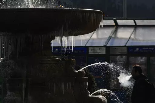 A pedestrian walks past a partially frozen fountain in New York, Tuesday, Jan. 11, 2022. A mass of arctic air swept into the Northeast on Tuesday, bringing bone-chilling sub-zero temperatures and closing schools across the region for the second time in less than a week. (AP Photo/Seth Wenig)