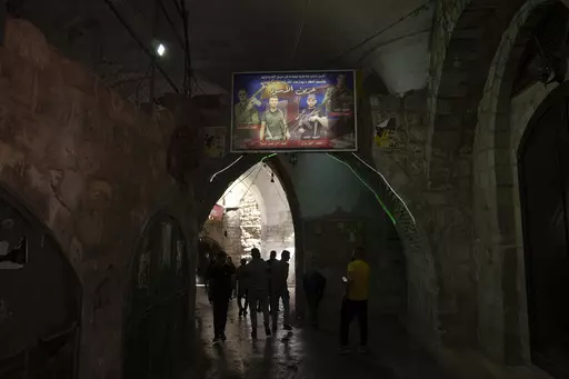 Palestinians walk under a banner depicting militants from the Lions' Den group who were killed by Israeli forces, from left, Fadi Qufesheh, Abdulrahman Soboh, Mohammad Azizi and Mahmoud Zakari, in al-Yasmeena quarter of the Old City of Nablus, in the West Bank, Thursday, May 4, 2023. The killing of Zuhair al-Ghaleeth last month, the first slaying of a suspected Israeli intelligence collaborator in the West Bank in nearly two decades, has laid bare the weakness of the Palestinian Authority and th
