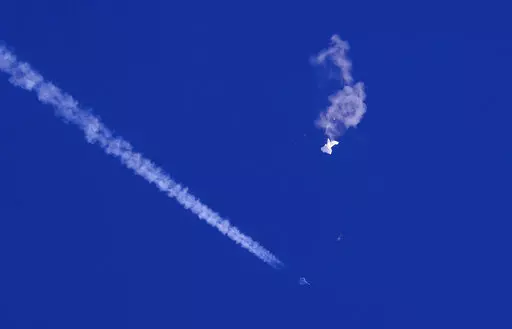 In this photo provided by Chad Fish, the remnants of a large balloon drift above the Atlantic Ocean, just off the coast of South Carolina, with a fighter jet and its contrail seen below it, Saturday, Feb. 4, 2023. The downing of the suspected Chinese spy balloon by a missile from an F-22 fighter jet created a spectacle over one of the state's tourism hubs and drew crowds reacting with a mixture of bewildered gazing, distress and cheering. (Chad Fish via AP)