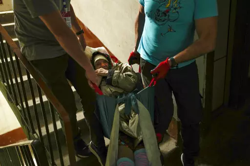 Roman Zhylenkov, left, and another volunteer of Vostok SOS charitable organisation carry an elderly woman from her home during an evacuation in Kramatorsk, eastern Ukraine, Thursday, May 26, 2022. Volunteer drivers are risking everything to deliver humanitarian aid to Ukrainians behind the front lines of the war — and to help many of them escape. The routes are dangerous and long and the drivers risk detention, injury or death. (AP Photo/Francisco Seco)