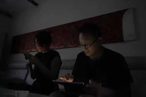 Wang Quanzhang and his wife Li Wenzu look at their phone and laptop in the dark after power was cut off for their apartment in Beijing's Changping district, Tuesday, June 20, 2023. Disbarred human rights lawyer Wang Quanzhang has been forced to move 13 times in two months as part of a pattern of harassment against him and three other prominent rights advocates in Beijing that is further squeezing the country's battered civil rights community. (AP Photo/Ng Han Guan)