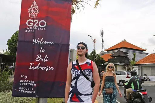 Tourists walk past a G20 banner in Nusa Dua, Bali, Indonesia on Friday, Nov. 11, 2022. The dozens of world leaders and other dignitaries traveling to Bali for the G-20 summit will be drawing a welcome spotlight on the revival of the tropical island's ailing tourism sector after a two-year closure to foreign travelers due to the pandemic. (AP Photo/Firdia Lisnawati)
