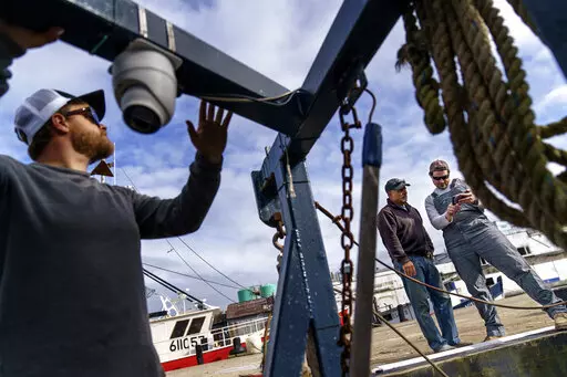 Mark Hager, left, positions a camera with the help of Anthony Lucia, right, as captain Al Cottone watches the feed on a monitor from his boat, the Sabrina Maria, in Gloucester, Mass., May 11, 2022. Hager's Maine-based startup, New England Maritime Monitoring, is one of a bevy of companies seeking to help commercial vessels comply with new federal mandates aimed at protecting dwindling fish stocks. But taking the technology overseas, where the vast majority of seafood consumed in the U.S. is caug