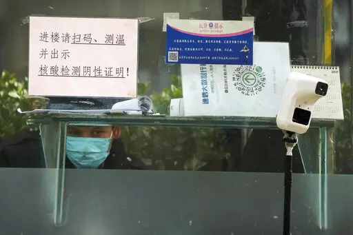 A security guard keeps watch inside a booth displaying a temperature scan device and a travel QR code, outside an office building in Beijing, Monday, Dec. 12, 2022. China will drop a travel tracing requirement as part of an uncertain exit from its strict "zero-COVID" policies that have elicited widespread dissatisfaction. (AP Photo/Andy Wong)