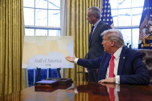 President Donald Trump gestures to a poster reading "Gulf of America" as Health and Human Services Secretary Robert F. Kennedy Jr., watches in the Oval Office at the White House in Washington, Tuesday, Feb. 25, 2025. (Pool via AP)