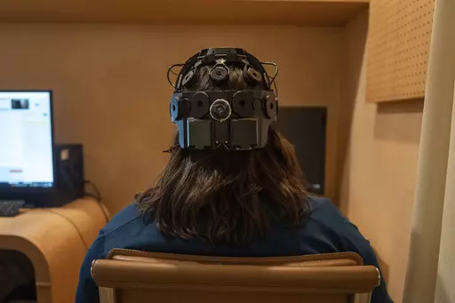 Emily Hollenbeck, a deep brain stimulation therapy patient, demonstrates an EEG device that records brain activity as she reacts to short videos at Mount Sinai’s “Q-Lab” in New York on Dec. 20, 2023. Dr. Brian Kopell, who directs Mount Sinai's Center for Neuromodulation, says in normal brains electrical activity reverberates unimpeded in all areas, in a sort of dance. In depression, the dancers get stuck within the brain’s emotional circuitry. DBS seems to “unstick the circuit,” he s