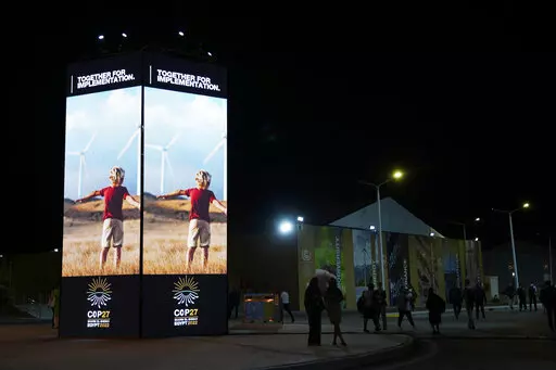 People walk past image of wind turbines at the COP27 U.N. Climate Summit, Tuesday, Nov. 8, 2022, in Sharm el-Sheikh, Egypt. (AP Photo/Peter Dejong, File)