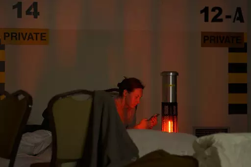 A woman looks at her mobile phone in a hotel underground parking turned into a bomb shelter during an air raid alert in Kyiv, Ukraine, Sunday, Feb. 27, 2022. Terrified men, women and children sought safety inside and underground, and the government maintained a 39-hour curfew to keep people off the streets as more than 150,000 Ukrainians fled to neighboring countries and the United Nations warned the number could grow to 4 million if fighting escalates.(AP Photo/Vadim Ghirda)