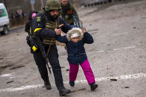 A Ukrainian police officer runs while holding a child as the artillery echoes nearby, while fleeing Irpin on the outskirts of Kyiv, Ukraine, Monday, March 7, 2022. (AP Photo/Emilio Morenatti)