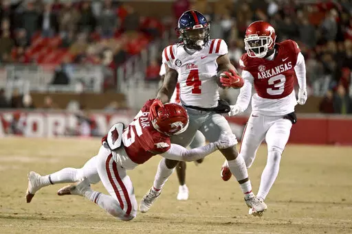 Mississippi running back Quinshon Judkins (4) is tackled by Arkansas defenders Simeon Blair (15) and Dwight McGlothern (3) during the first half of an NCAA college football game Saturday, Nov. 19, 2022, in Fayetteville, Ark. (AP Photo/Michael Woods)