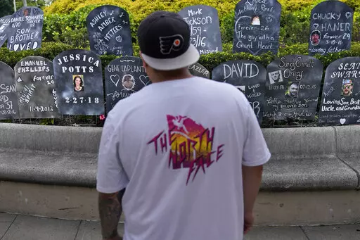A man looks at cardboard gravestones with the names of victims of opioid abuse outside the courthouse where the Purdue Pharma bankruptcy is taking place in White Plains, N.Y., Monday, Aug. 9, 2021.  A federal appeals panel is scheduled to hear arguments on whether members of the Sackler family can be granted protection from lawsuits as part of a bankruptcy settlement for the company they own, OxyContin maker Purdue Pharma. If the company doesn’t get what it wants, it could have to fight off th