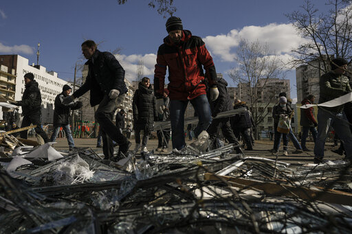 People clear debris outside a medical center damaged after parts of a Russian missile, shot down by Ukrainian air defense, landed on a nearby apartment block, according to authorities, in Kyiv, Ukraine, Thursday, March 17, 2022. Russian forces destroyed a theater in Mariupol where hundreds of people were sheltering Wednesday and rained fire on other cities, Ukrainian authorities said, even as the two sides projected optimism over efforts to negotiate an end to the fighting. (AP Photo/Vadim Ghird