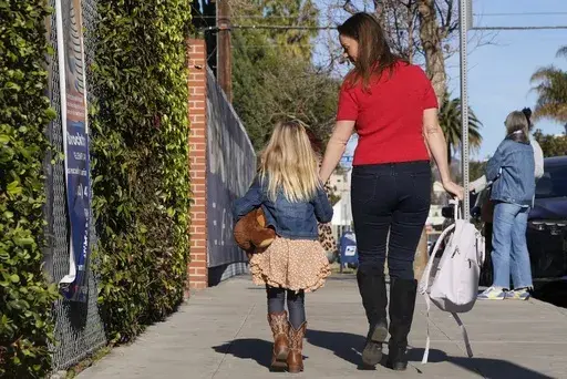 Kelli Ferrone walks her daughter into a temporary school Friday, Jan. 24, 2025, in Los Angeles, as they wait for Canyon Charter Elementary School to reopen after being impacted by smoke and ash from the Palisades Fire. (AP Photo/Brittany Peterson)