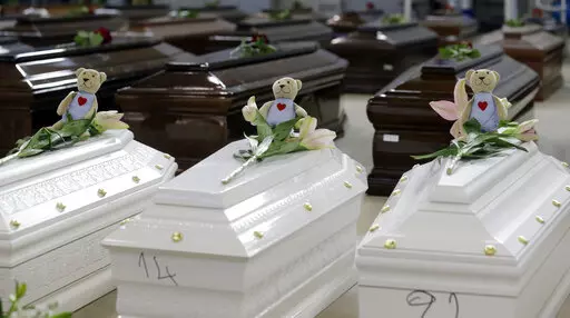 Teddy bears and flowers placed are placed on the coffins of deceased migrants inside a hangar at Lampedusa's airport, Italy, Saturday, Oct. 5, 2013. A decade ago this year, the head of the EU's executive branch, Jose Manuel Barroso stood visibly shaken before hundreds of coffins holding the corpses of migrants drowned off the Italian Island of Lampedusa. (AP Photo/Luca Bruno, File)