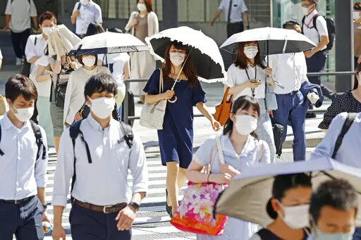 People, some of them holding parasols, cross an intersection amid heat, in Tokyo, Monday, June 27, 2022.  Japan’s government issued a warning for possible power crunch in the Tokyo area Monday, asking offices and residents to save energy as the capital region is hit by sweltering heat, with weather officials announcing an earliest end to the rainy season in decades. (Yusuke Ogata/Kyodo News via AP)