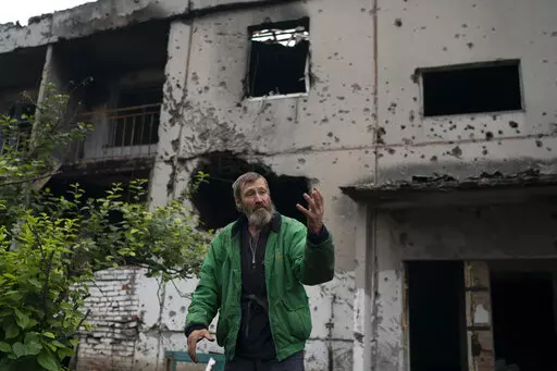 Viacheslav Myronenko, 71, stands in front of the entrance of a damaged building where he lives in the freed village of Hrakove, Ukraine, Tuesday, Sept. 13, 2022. Myronenko has been living in the basement of his bombed-out apartment building with three neighbors for more than four months. (AP Photo/Leo Correa)