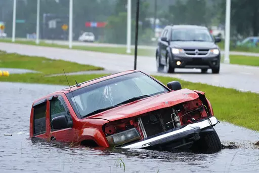 An abandoned vehicle is half submerged in a ditch next to a near flooded highway as the outer bands of Hurricane Ida arrive Sunday, Aug. 29, 2021, in Bay Saint Louis, Miss. (AP Photo/Steve Helber)