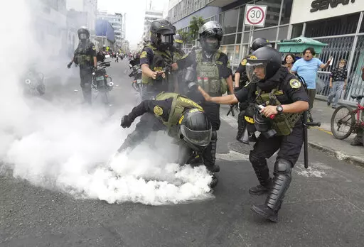 Police officers pick up a tear gas canister that was thrown back at them by anti-government protesters who traveled to the capital from across the country to march against Peruvian President Dina Boluarte in Lima, Peru, Wednesday, Jan. 18, 2023. Protesters are seeking immediate elections, Boluarte's resignation, the release of ousted President Pedro Castillo and justice for the dozens of protesters killed in clashes with police. (AP Photo/Martin Mejia)