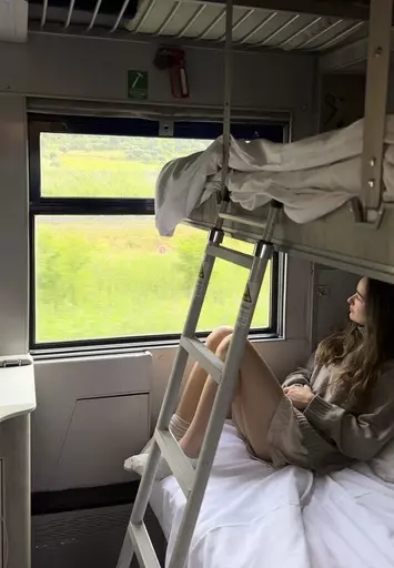 Sarah Marks, of London, looks out at the Italian countryside on TrenItalia's Intercity Notte sleeper train from Palermo to Rome, on June 10, 2023. A growing number of climate-conscious Europeans are giving up flying in favor of long-haul trains. (Sarah Marks via AP)