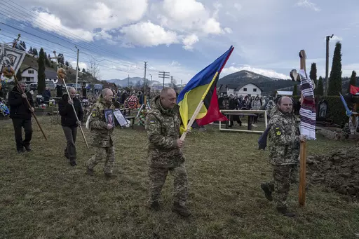 Ukrainian servicemen carry national flags and photos of their comrade Vasyl Boichuk who was killed in Mykolayiv in March 2022, during his funeral ceremony at the cemetery in Iltsi village, Ukraine, Tuesday, Dec. 26, 2023. (AP Photo/Evgeniy Maloletka)