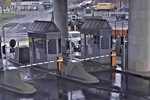 In this image taken from security video, a light colored vehicle, top center, flies over a fence into the Rainbow Bridge customs plaza, Wednesday, Nov. 22, 2023, in Niagara Falls, N.Y. A vehicle exploded at a checkpoint on the American side of a U.S.-Canada bridge in Niagara Falls Wednesday, leaving two people dead and prompting the closing of four border crossings in the area, authorities said. (Customs Border Protection via AP)