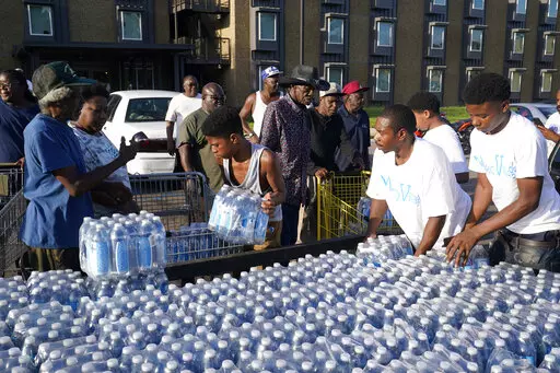 Residents of the Golden Keys Senior Living apartments flock to a trailer full of water being delivered by the AIDS Healthcare Foundation in Jackson, Miss., Thursday, Sept. 1, 2022. A recent flood worsened Jackson's long standing water system problems. (AP Photo/Steve Helber)