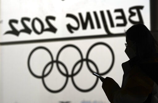 A woman looks at her phone as she passes an Olympic logo inside the main media center for the 2022 Winter Olympics, Jan. 18, 2022, in Beijing. (AP Photo/David J. Phillip, File)