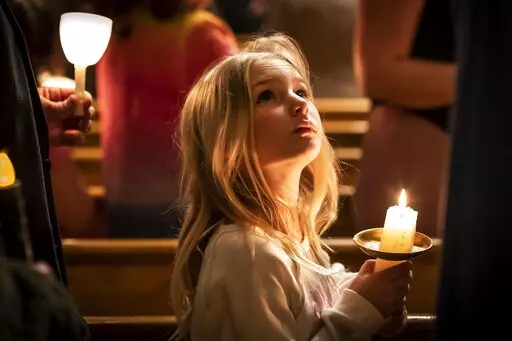 A girl looks at her mother while holding a candle during Good Friday service at St. Mary's Ukrainian Orthodox Cathedral, Friday, April 22, 2022, in Allentown, Pa.. While Easter is the most joyous of holy days on the church calendar, marking the day Christians believe Jesus triumphed over death, many members of Ukrainian Orthodox churches across the United States are finding it difficult to summon joy at a time of war. (AP Photo/Wong Maye-E)