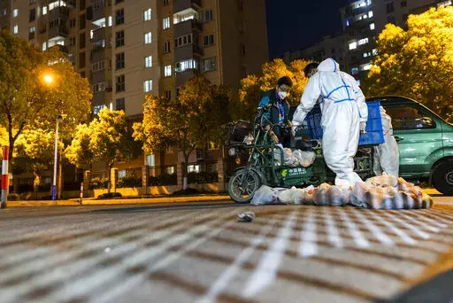 Deliverymen wearing protective suits carry bags of food at the gate of a residential community in Shanghai, China, Monday, April 11, 2022. The U.S. has ordered all non-emergency consular staff to leave Shanghai, which is under a tight lockdown to contain a COVID-19 surge. Many residents in the city of 26 million have been confined to their homes for up to three weeks as China maintains its "zero-COVID" strategy of handling outbreaks with strict isolation and mass testing. (AP Photo)