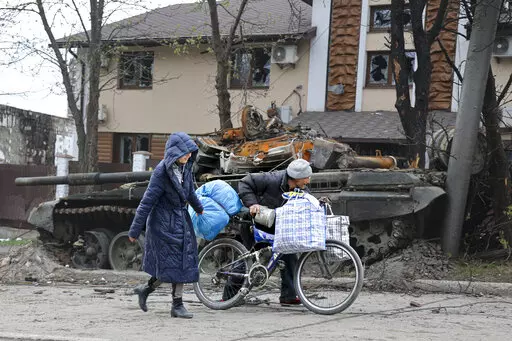 Local civilians walk past a tank destroyed during heavy fighting in an area controlled by Russian-backed separatist forces in Mariupol, Ukraine, Tuesday, April 19, 2022. Taking Mariupol would deprive Ukraine of a vital port and complete a land bridge between Russia and the Crimean Peninsula, seized from Ukraine from 2014. (AP Photo/Alexei Alexandrov)