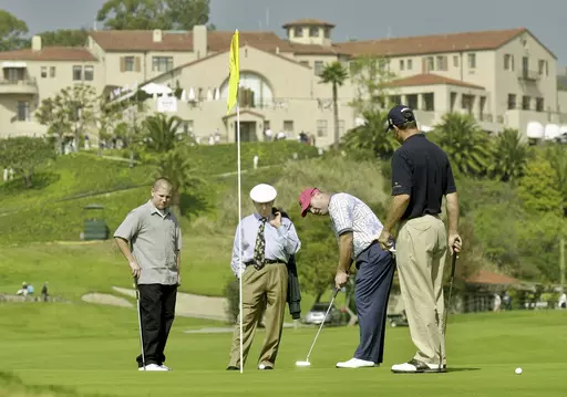 With the historic clubhouse in the background, Duffy Waldorf takes a practice putt at the 10th green as veteran teaching pro Eddie Merrins, in the tie, and golfer Arron Oberholser, right, watch during a practice session for the Nissan Open at Riviera Country Club, Feb. 18, 2003, in Los Angeles. Merrins died Wednesday, Nov. 22, 2023, at age 91. (AP Photo/Reed Saxon, File)
