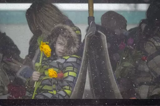 A refugee child fleeing the conflict from neighbouring Ukraine holds flowers, given out to celebrate International Women's Day, as he sits on a bus, at the Romanian-Ukrainian border, in Siret, Romania, Tuesday, March 8, 2022. It is a global day to celebrate women, but many fleeing Ukraine feel only the stress of finding a new life for their children as husbands, brothers and fathers stay behind to defend their country from Russia's invasion. (AP Photo/Andreea Alexandru)