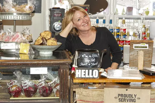 Cafe owner Maureen Donnelly Morris is shown behind the counter at Back Street Brews, on Dec. 16, 2021, in Lovettsville, Va., a gathering spot where neighbors of all political persuasions come together for coffee and civil chat. In the neighborhood, the mix of pro-Trump signs, gay-pride rainbow flags and Black Lives Matter banners speaks to a striking diversity in political views and an undercurrent of tension that plays out unfiltered on Facebook. But in this "coffee bubble," left, right, red an