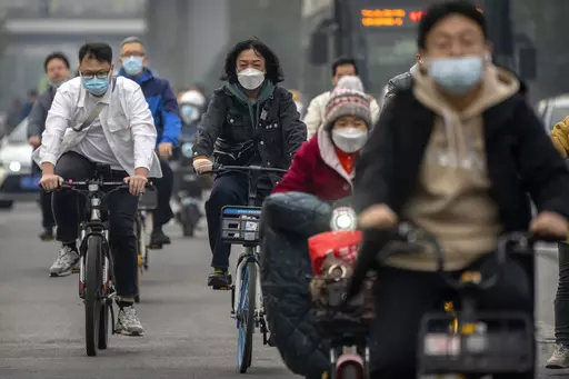 Commuters wearing face masks ride bicycles along a street in the central business district in Beijing, Thursday, Oct. 20, 2022. The World Health Organization downgraded its assessment of the coronavirus pandemic on Friday, May 5, 2023, saying it no longer qualifies as a global emergency. (AP Photo/Mark Schiefelbein, File)