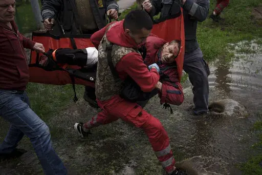 An emergency worker is helped by locals to carry an injured man who missing a part of his leg to an ambulance following a Russian bombardment in Kharkiv, Ukraine, Wednesday, April 27, 2022. (AP Photo/Felipe Dana)