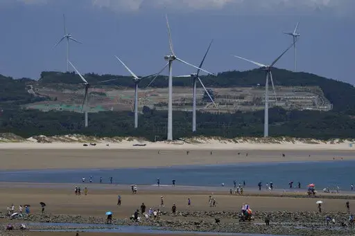 Beachgoers walk near wind turbines along the coast of Pingtan in Southern China's Fujian province, on Aug. 6, 2022. The world's two biggest emitters of greenhouse gases are sparring on Twitter over climate policy, with China asking if the U.S. can deliver on the landmark climate legislation signed into law by President Joe Biden this week. (AP Photo/Ng Han Guan)