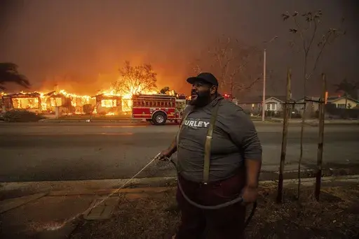 A resident sprays their property with a garden hose as the Eaton Fire engulfs structures across the street, Wednesday, Jan. 8, 2025 in Altadena, Calif. (AP Photo/Ethan Swope, File)