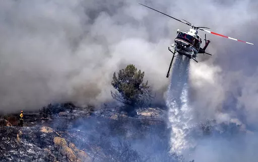 A firefighter is dwarfed by an aerial drop at the the Chaparral Fire in Murrieta which still blazes, Sunday, August 29, 2021. Several homes appear to be evacuated in the area. (Cindy Yamanaka/The Orange County Register via AP)