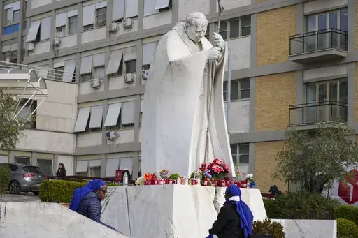 Nuns sit next to a statue of Pope John Paul II in front of the Agostino Gemelli Polyclinic, in Rome, Monday, Feb. 17, 2025, where Pope Francis has been hospitalized to undergo some necessary diagnostic tests and to continue his ongoing treatment for bronchitis. (AP Photo/Andrew Medichini)