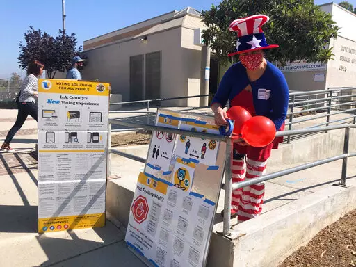 Camille Teran-Grange, a volunteer at polling place at the Montecito Heights Senior Citizen Center in Los Angeles, adds balloons to voter information placards on Tuesday, Sept. 14, 2021. (AP Photo/Stefanie Dazio)